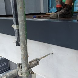 GOL MAR - Montaż obróbki blacharskiej na ocieplonym poddaszu z użyciem wiertarki, widoczne rusztowanie i materiały izolacyjne Tyron