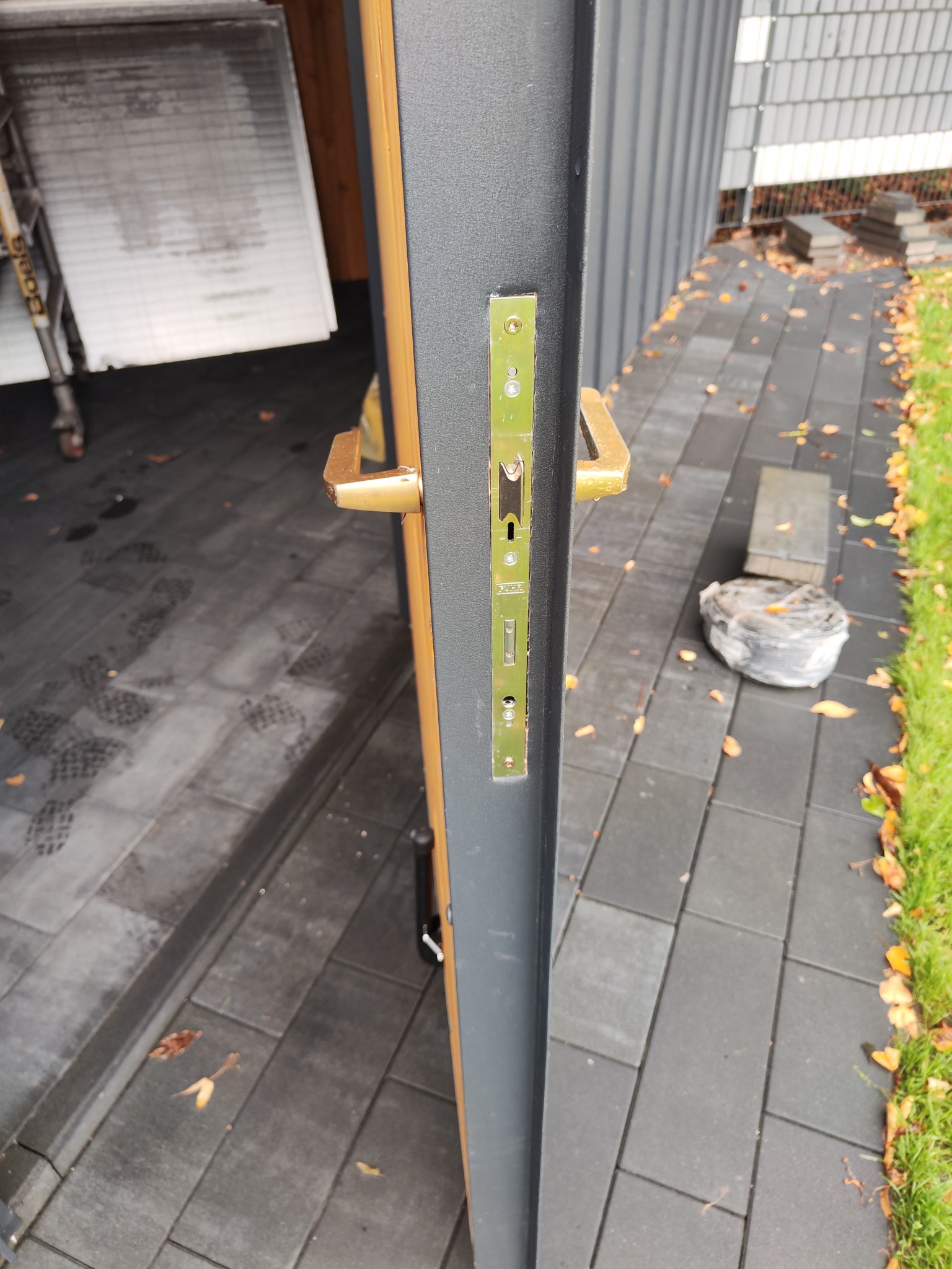 Otwarta brama garażowa z widocznym zamkiem i fragmentem kostki brukowej na zewnątrz. Lekko pochmurne oświetlenie.