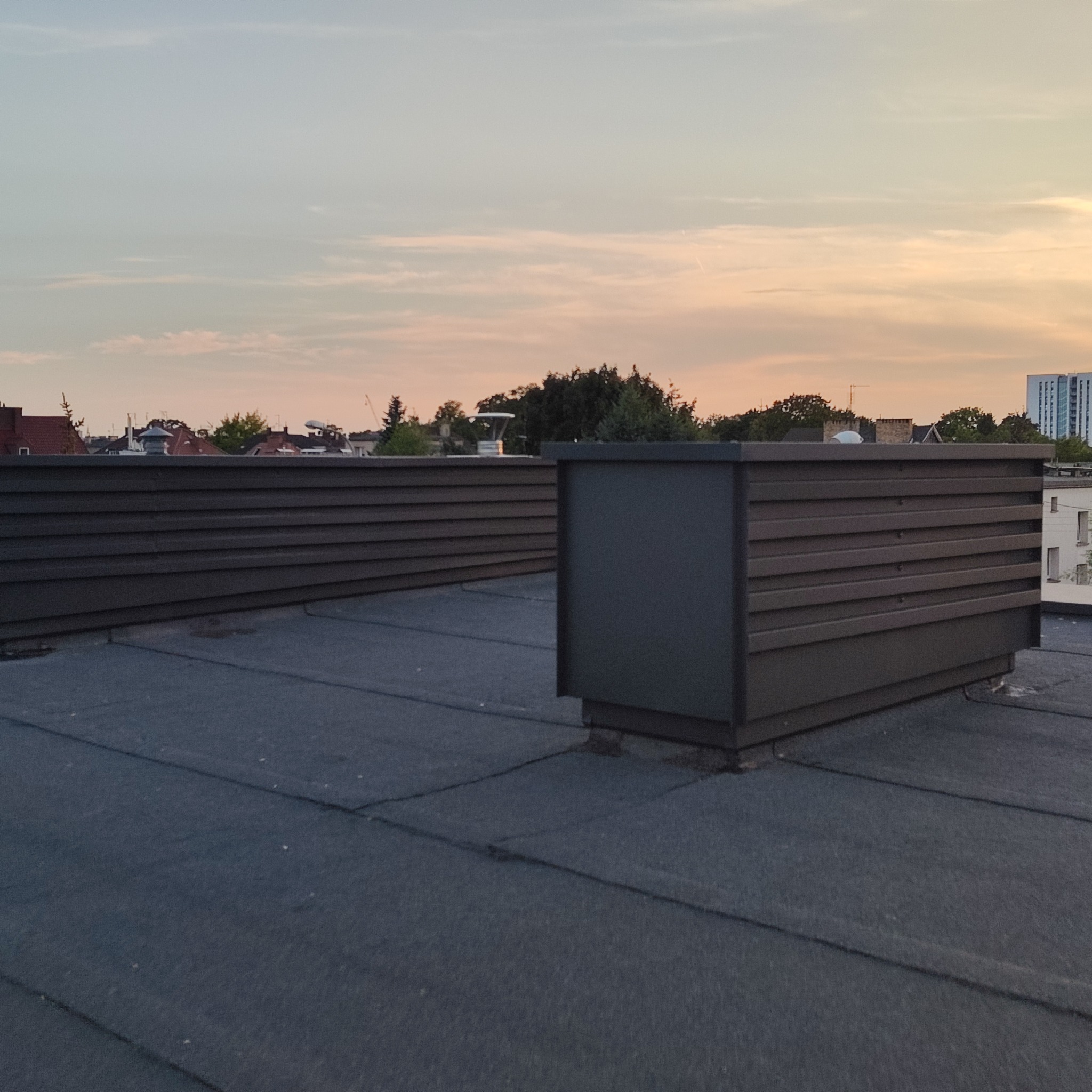 Wykończony dach płaski z obróbkami blacharskimi w Pogorzeli. Widoczne elementy wentylacyjne i konstrukcja dachu na tle zachodzącego słońca.