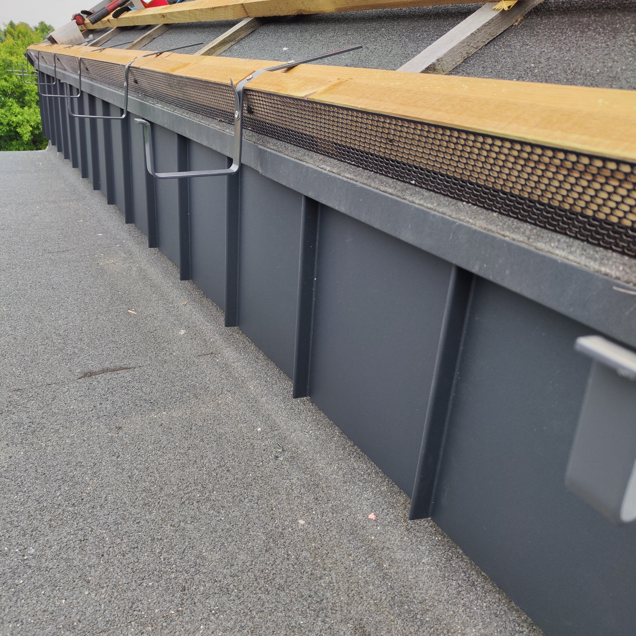 Szary dach z nową obróbką blacharską i siatką zabezpieczającą przed liśćmi, widok z góry pod kątem.