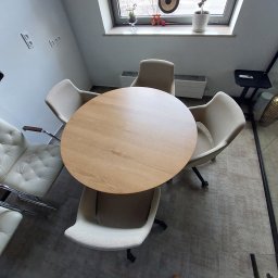 Global Labs sp. z o.o. - Jasne wnętrze z okrągłym, drewnianym stołem otoczonym krzesłami w odcieniach beżu i bieli. Widok z góry, ukazujący minimalistyczny design i neutralną kolorystykę.