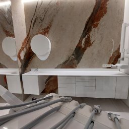 Global Labs sp. z o.o. - Nowoczesne wnętrze gabinetu z długim białym blatem, umywalką i ścianą z marmurowym wzorem. Widoczne okrągłe podświetlane lustra i fragment sprzętu medycznego.