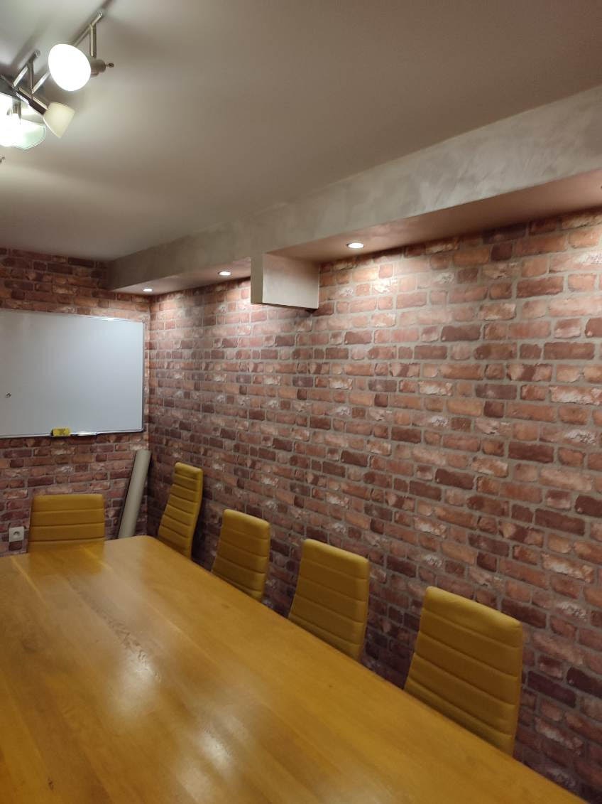 Biuro po remoncie: ściana z cegły, drewniany stół, żółte krzesła. Nowoczesne oświetlenie sufitowe. Czyste, jasne wnętrze, idealne do pracy.
