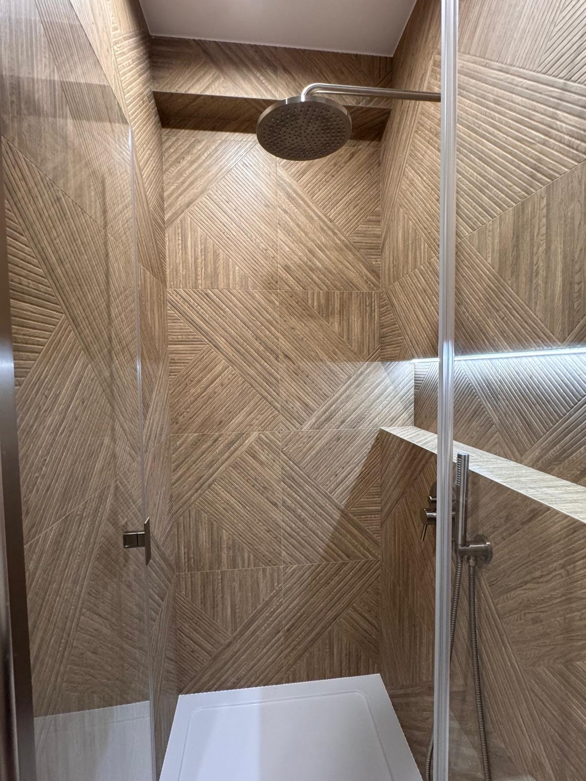 Kabina prysznicowa z deszczownicą i geometrycznymi płytkami imitującymi drewno. Nowoczesny design z podświetleniem LED. Widok z dołu na górę.