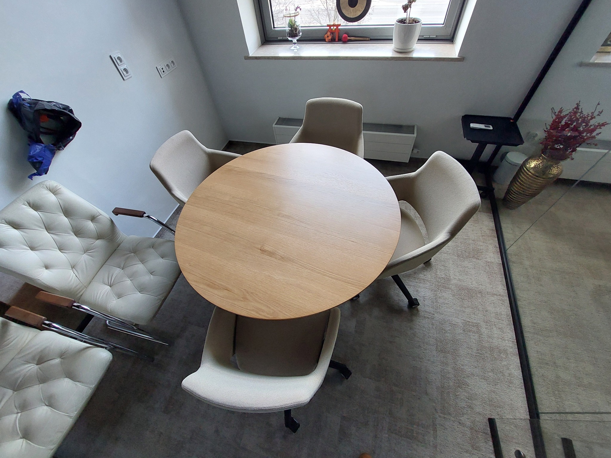 Jasne wnętrze z okrągłym, drewnianym stołem otoczonym krzesłami w odcieniach beżu i bieli. Widok z góry, ukazujący minimalistyczny design i neutralną kolorystykę.