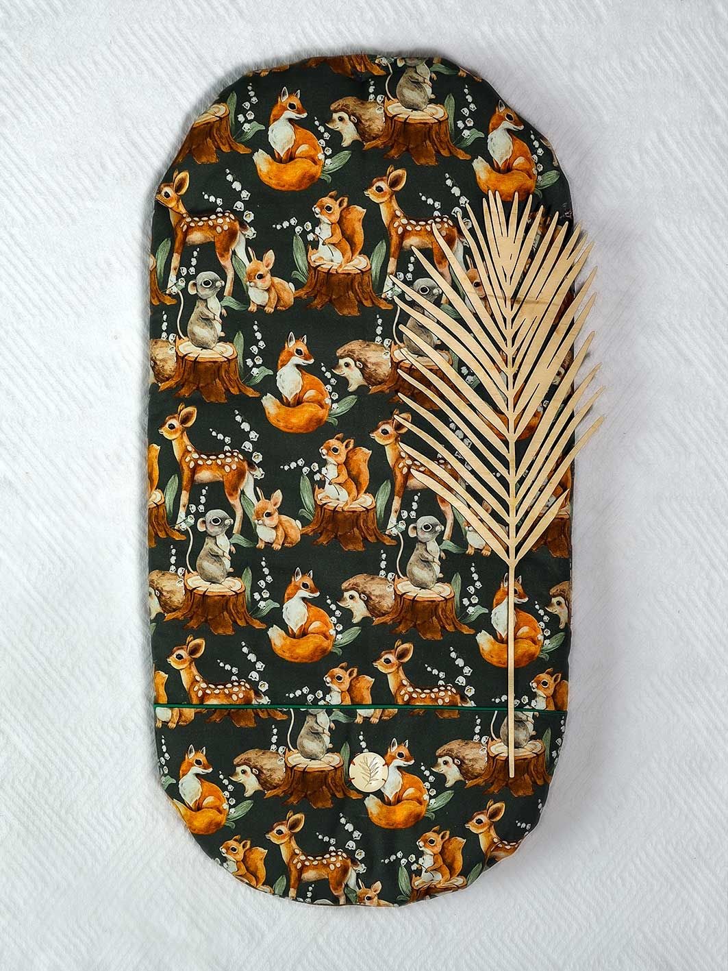 Owalna podkładka z motywem leśnych zwierząt (lis, jeż, sarna, wiewiórka, mysz) na ciemnozielonym tle, dekorowana złotą gałązką na białym tle.