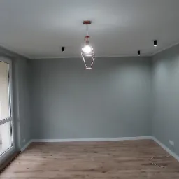 Wnętrze pokoju po remoncie: szare ściany, panele podłogowe, okno balkonowe i designerskie lampy wiszące