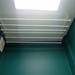 JACO Bud&Art Jacek Kozina - Zamontowana pod sufitem suszarka na pranie, ściany pomalowane na ciemny, morski kolor, widoczny fragment kratki wentylacyjnej.