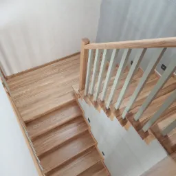 Jasne drewniane schody z kremowymi balustradami i poręczą, widok z góry, nowoczesne wykończenie.