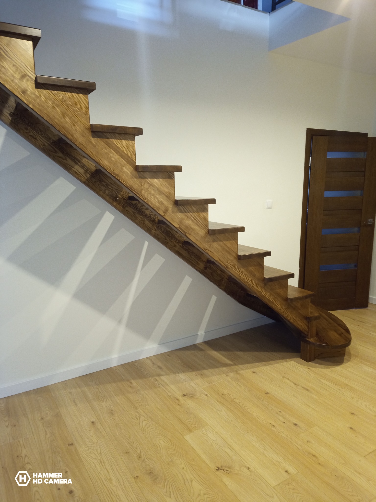 Nowoczesne, dębowe schody z zaokrąglonym stopniem startowym, prowadzące na górę, obok widoczne drzwi z przeszkleniami.