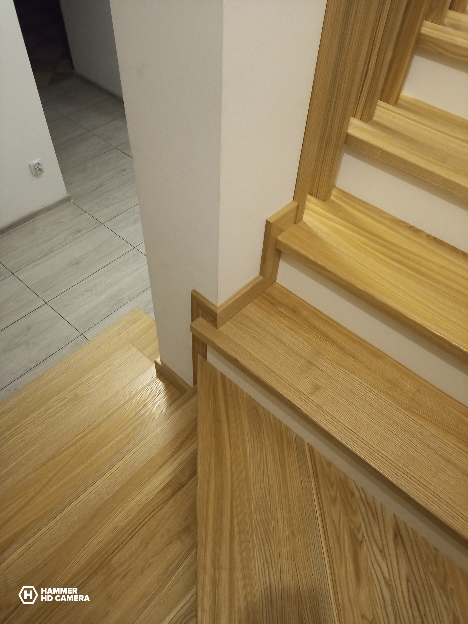 Jasne, dębowe stopnie schodów z widocznym usłojeniem drewna, przylegające do białej ściany z drewnianym wykończeniem.