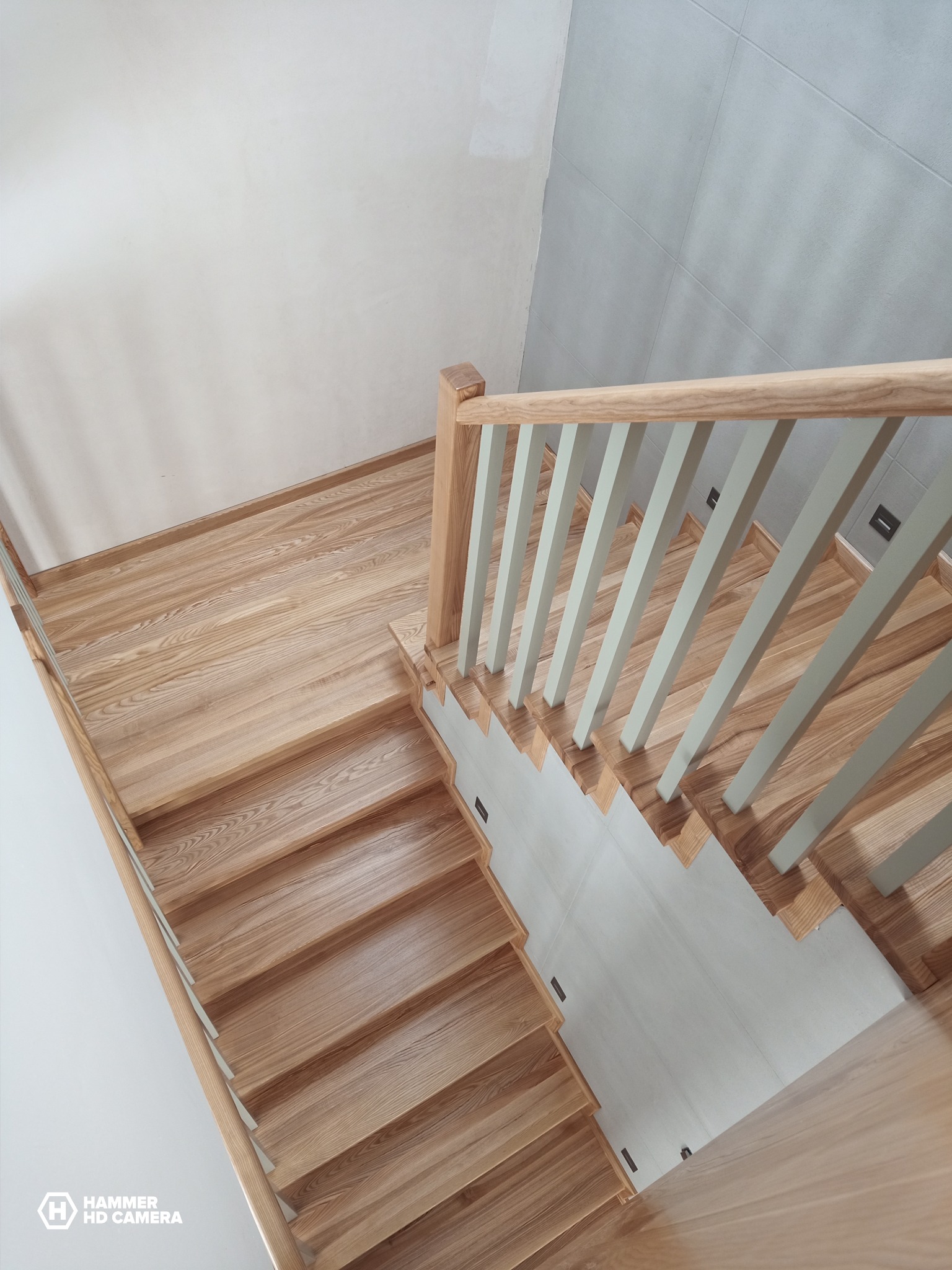 Jasne drewniane schody z kremowymi balustradami i poręczą, widok z góry, nowoczesne wykończenie.