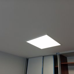 Usługi Remontowo Malarskie - Szary sufit z zamontowanym kwadratowym panelem LED, widoczne zabezpieczone taśmą malarską szafy przesuwne.