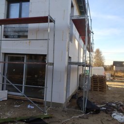 Usługi Remontowo Malarskie - Dom w trakcie ocieplania, widoczne rusztowania, styropianowe płyty elewacyjne oraz palety i gruz na ziemi.