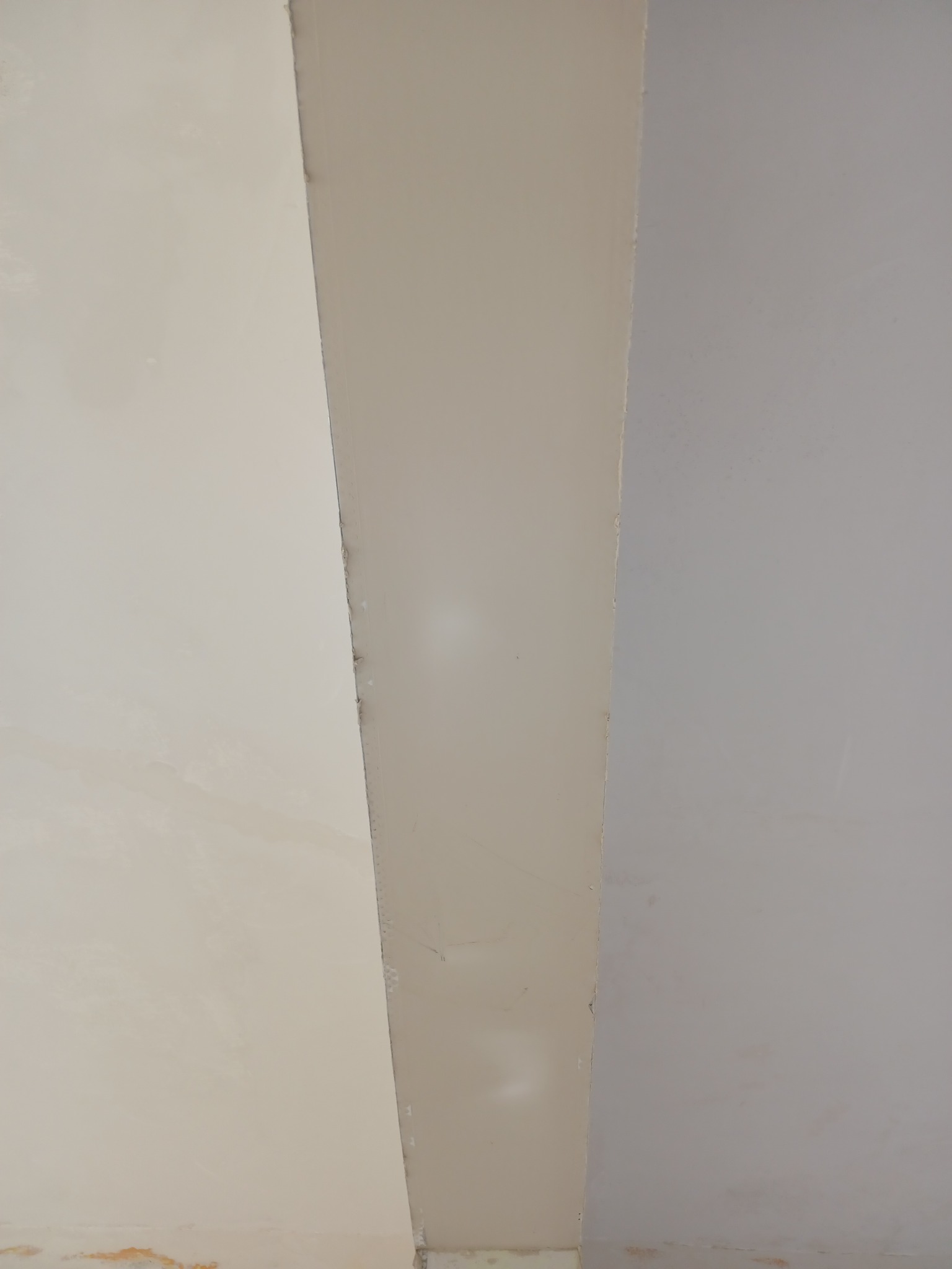 Fragment ściany z widocznymi śladami po niedokładnym położeniu gładzi i różnicami w odcieniach farby, ukazujący niedoskonałości wykończenia wnętrza.