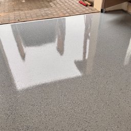 Silesia Boden - Błyszcząca, szara posadzka z drobnymi, kolorowymi wtrąceniami, odbijająca światło w garażu z otwartą bramą na zewnątrz.