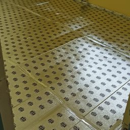 Andro-Bud - Przygotowanie podłoża pod posadzkę w pokoju z żółtymi ścianami, wyłożone maty izolacyjne z napisem 'CUTTING LINES', widoczne okno i fragment ściany z niedokończonym wykończeniem.