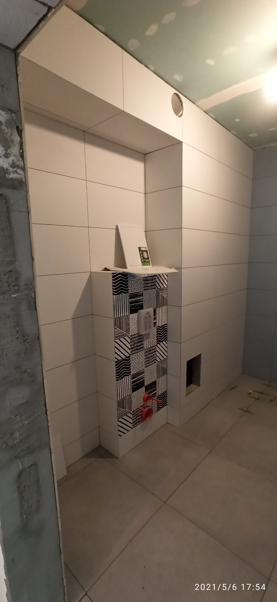 Łazienka w trakcie remontu: białe płytki ścienne, dekoracyjne płytki na zabudowie stelaża WC z przyciskiem, otwór wentylacyjny w suficie z płyt karton gips.