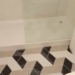 Nowoczesna łazienka z białą armaturą, kabiną prysznicową i podłogą w geometryczny wzór 3D w odcieniach bieli, beżu i czerni.