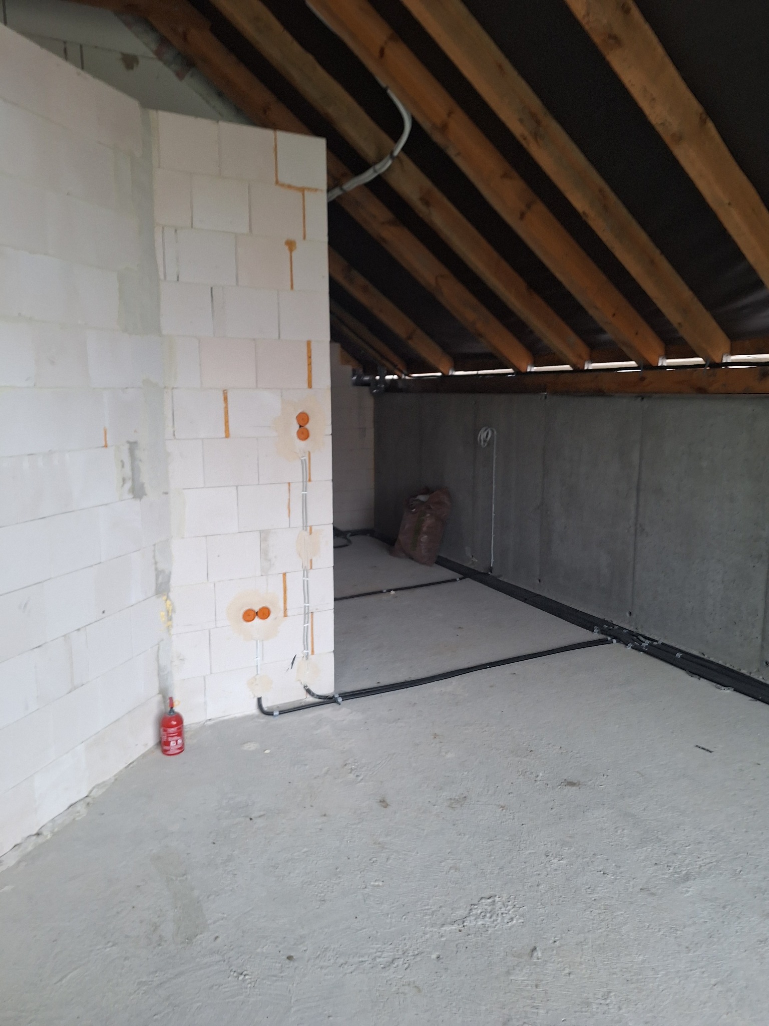 Surowy stan poddasza: instalacja elektryczna w peszlach na podłodze i w ścianach z betonu komórkowego. Widoczna drewniana konstrukcja dachu.