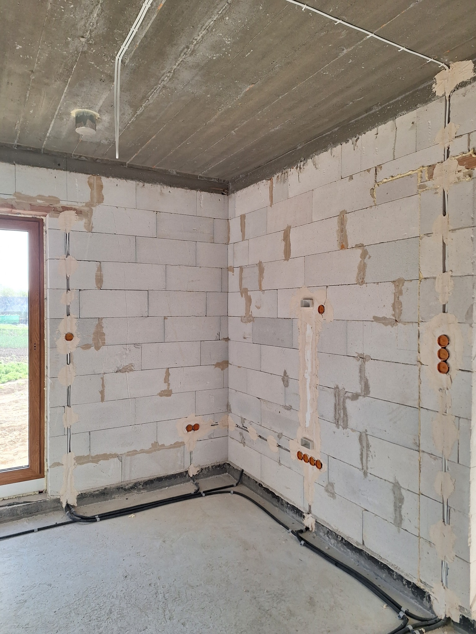 Wnętrze w surowym stanie z widocznymi przewodami elektrycznymi w ścianach z betonu komórkowego i pod sufitem. Widoczne puszki instalacyjne i kable przy podłodze.