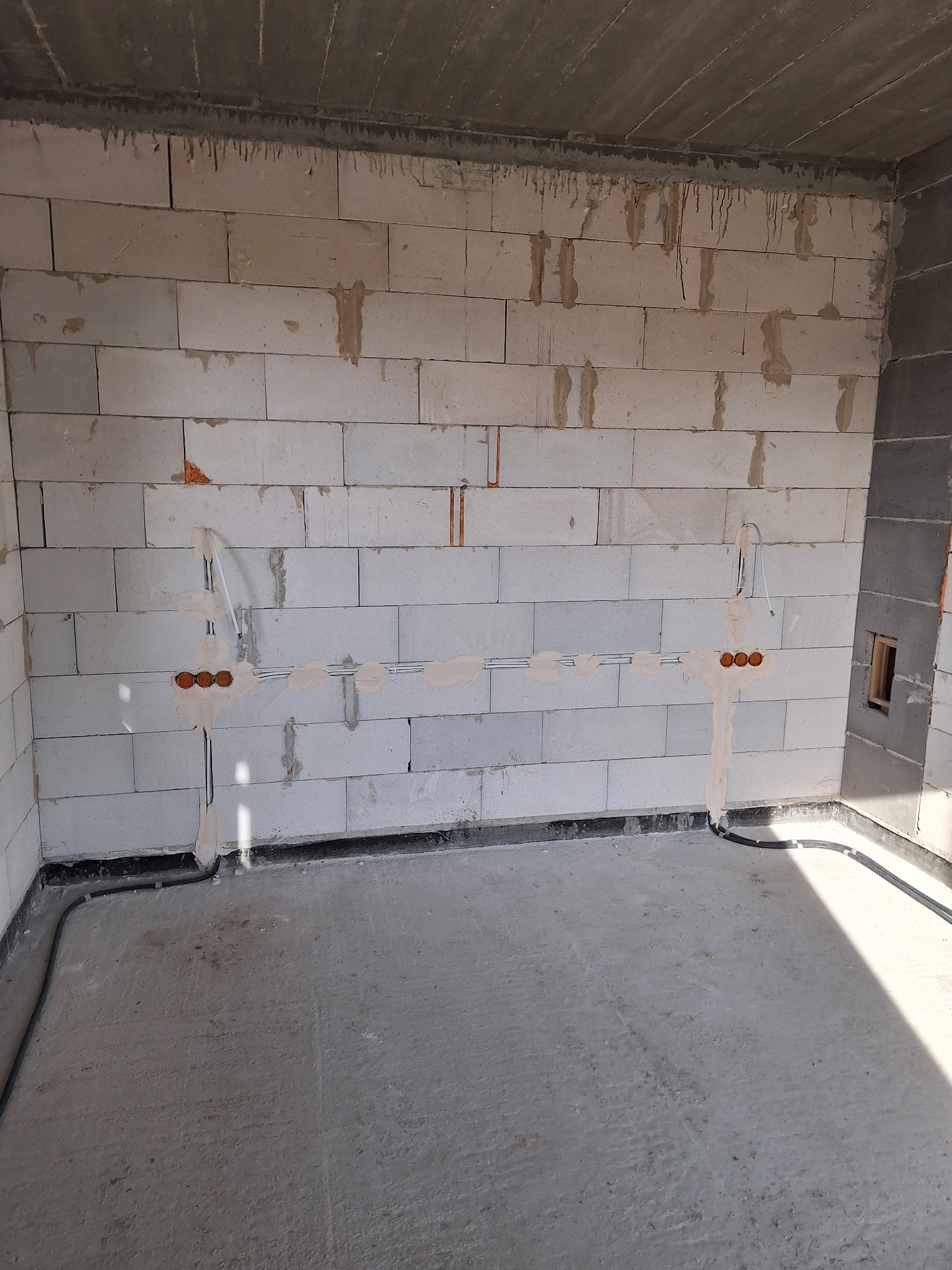 Ściana z instalacją elektryczną w surowym stanie: widoczne kable, puszki podtynkowe i przewody w ścianie z betonu komórkowego. Nowa instalacja przed tynkowaniem.