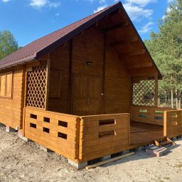 Tarasywwl - Nowa, drewniana, brązowa altana z kratownicą i małym tarasem, osadzona na betonowych bloczkach, na piaszczystym podłożu, z widocznymi drzewami w tle.