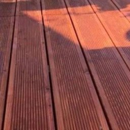 Tarasywwl - Deski tarasowe z ciemnego drewna, ryflowane, oświetlone popołudniowym słońcem, rzucające cień.