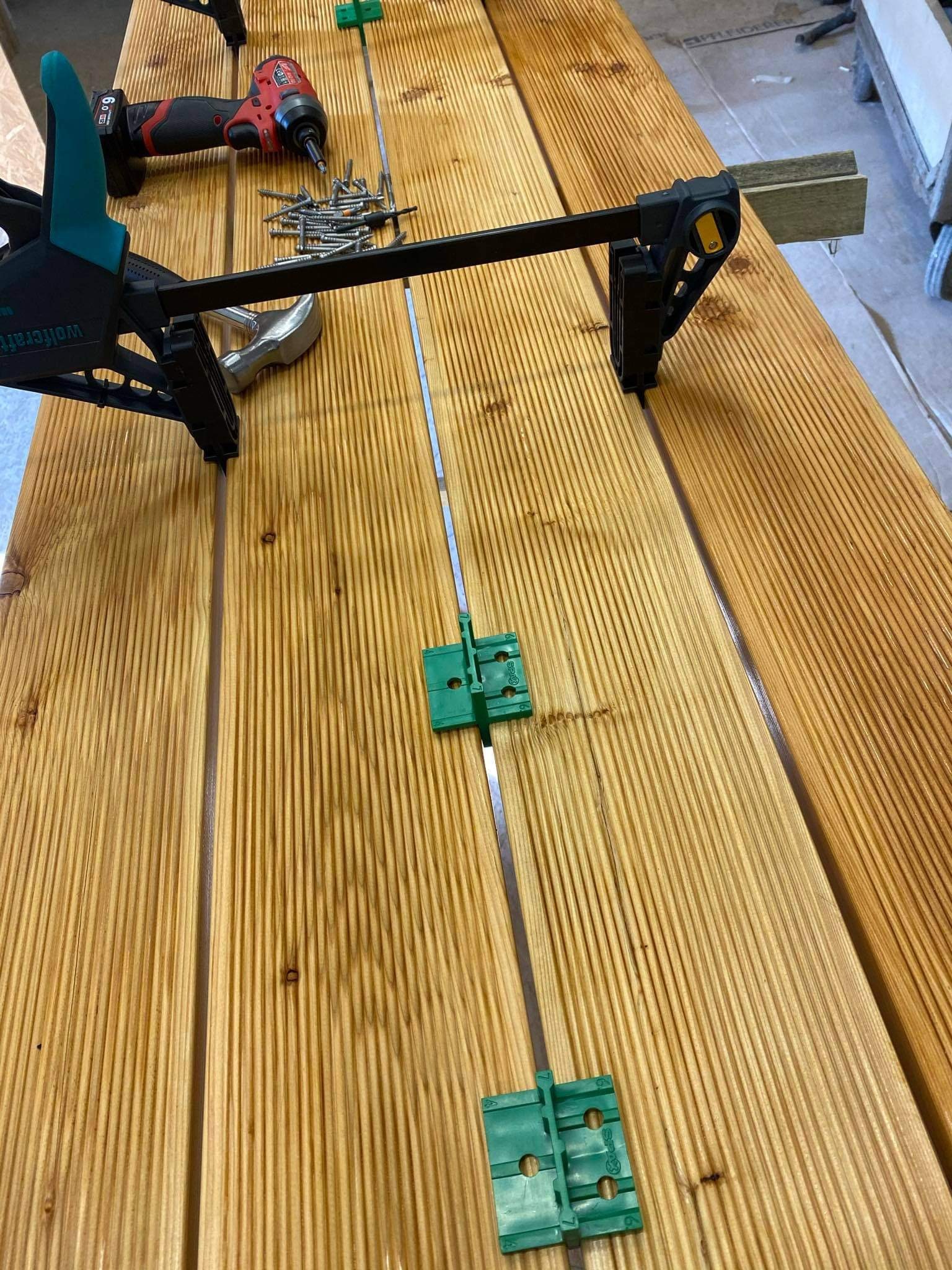 Montaż desek tarasowych z użyciem ścisków, wkrętarki i plastikowych dystansów, widoczne wkręty i młotek.