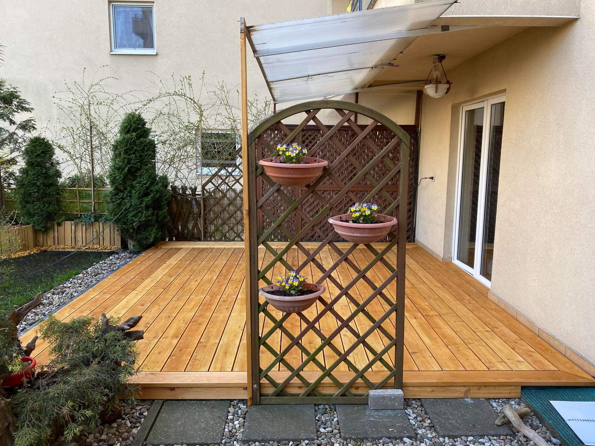 Zadaszony taras z drewna z kratką na kwiaty w doniczkach, obok domu.