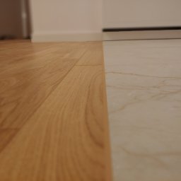 FloorWood Przemysław Wójcik - Połączenie jasnego parkietu z marmurową podłogą, widok z niskiej perspektywy, ukazujący strukturę drewna i żyłkowanie kamienia.