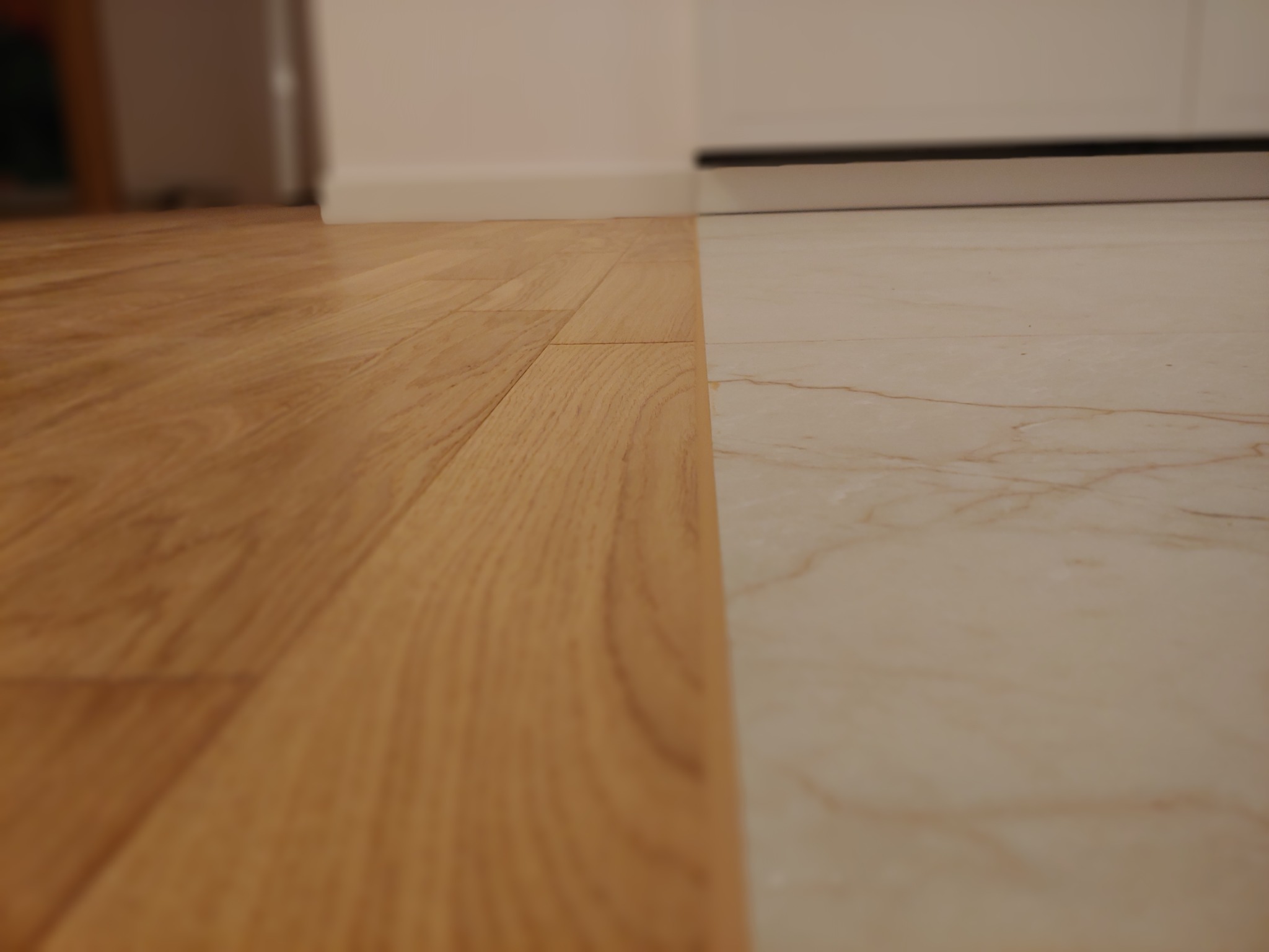 Połączenie jasnego parkietu z marmurową podłogą, widok z niskiej perspektywy, ukazujący strukturę drewna i żyłkowanie kamienia.