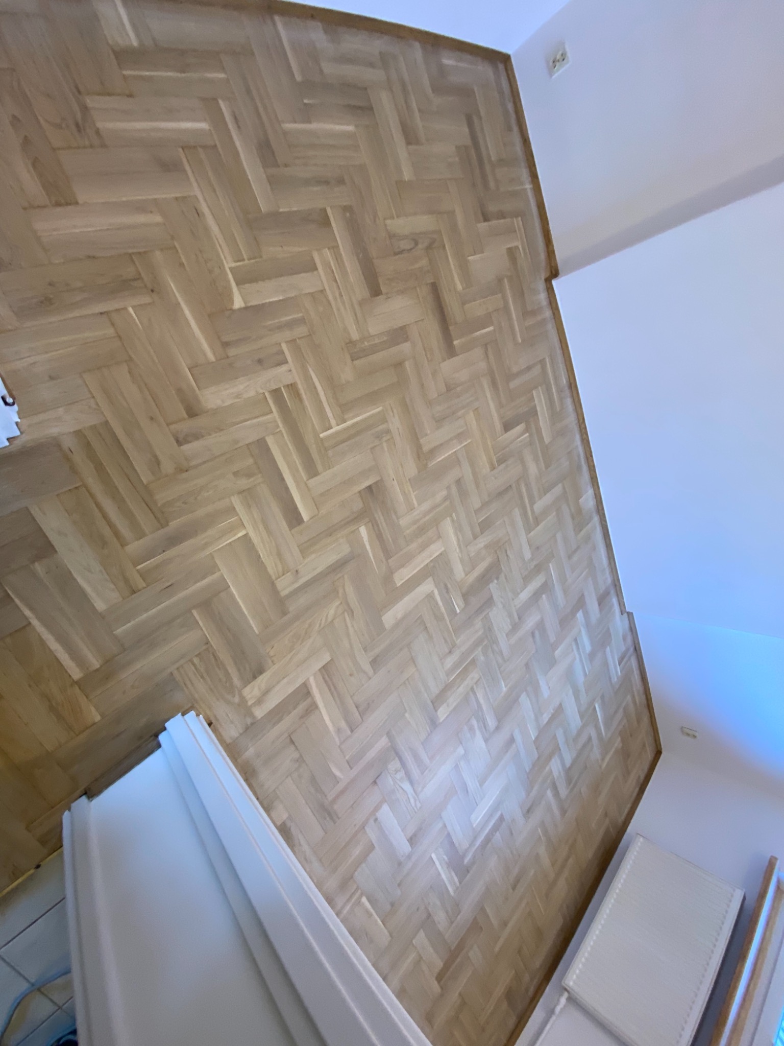 Ułożony parkiet w jodełkę francuską, jasne drewno, widok z góry, białe ściany i grzejnik.