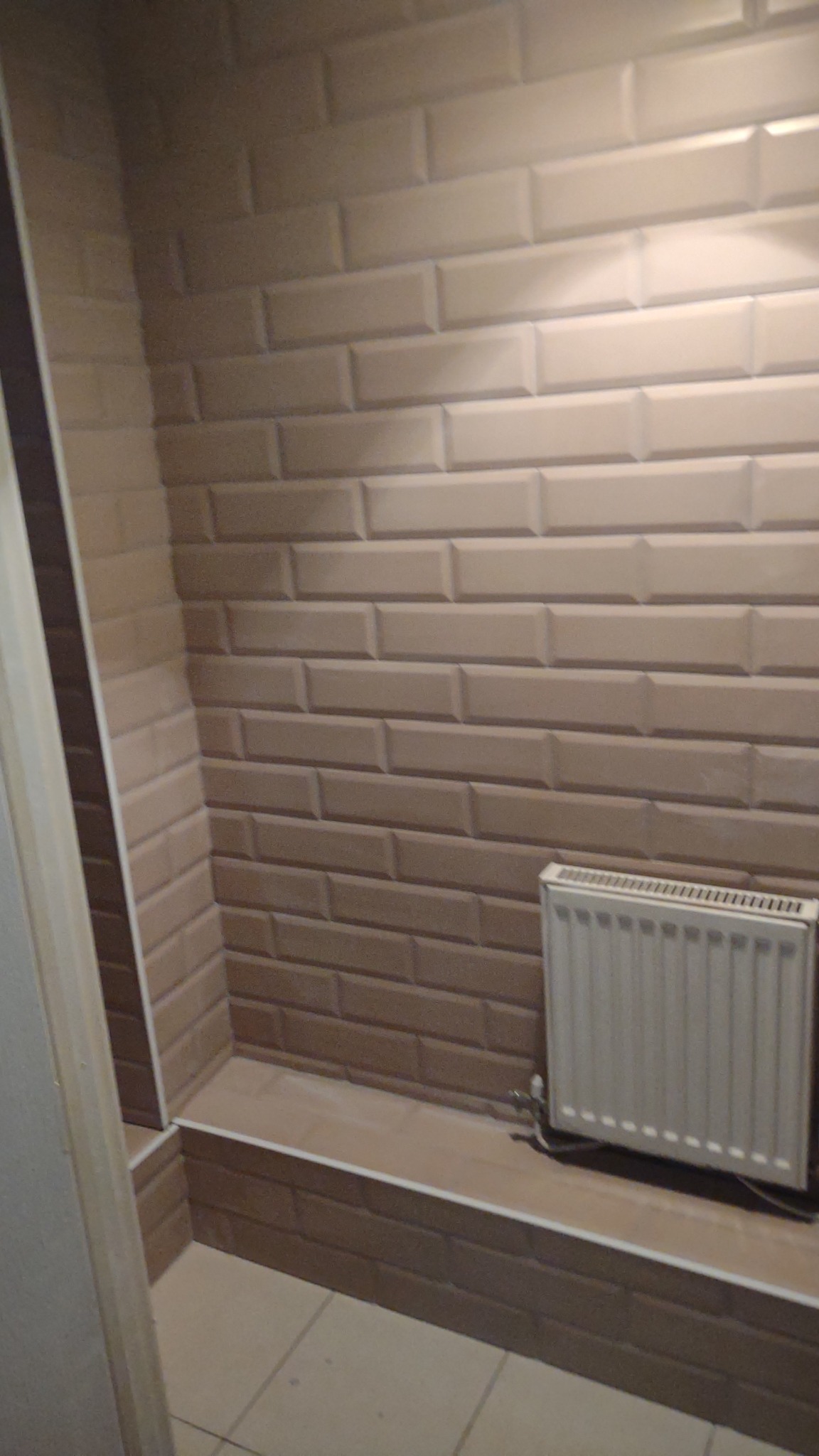 Beżowa, prostokątna glazura ułożona w rzędach na ścianie wnęki łazienkowej, widoczny grzejnik.