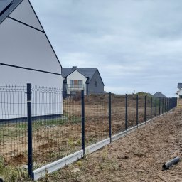 PPHU ROB-MAR Robert Marek - Nowoczesne ogrodzenie panelowe z podmurówką betonową, widok z boku na tle domów jednorodzinnych w pochmurny dzień. Słupki w kolorze grafitowym.