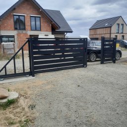 PPHU ROB-MAR Robert Marek - Nowoczesna, przesuwna brama wjazdowa z poziomymi panelami, zamontowana na posesji z domami w trakcie budowy. Widoczna siatka ogrodzeniowa i samochód osobowy.