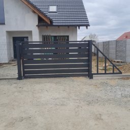 PPHU ROB-MAR Robert Marek - Nowoczesna, pozioma brama wjazdowa z metalowymi panelami w kolorze antracytowym, zamontowana przy domu z szarą elewacją i ogrodzeniem z siatki.