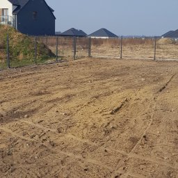 PPHU ROB-MAR Robert Marek - Nowoczesne ogrodzenie panelowe w kolorze grafitowym, otaczające teren budowy z widocznymi śladami opon. W tle domy jednorodzinne i błękitne niebo.