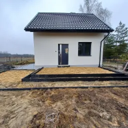 Przygotowanie terenu pod taras: obrzeża z tworzywa sztucznego i piasek kwarcowy przed nowoczesnym domem z czarnym dachem.