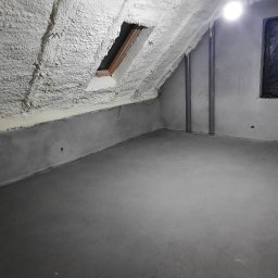 PMP-PUR Piotr Paczkowski - Poddasze po ociepleniu pianką PUR, widoczne krokwie i okno dachowe, sufit pokryty grubą warstwą pianki, ściany szare, rury pionowe, surowy stan wykończenia.