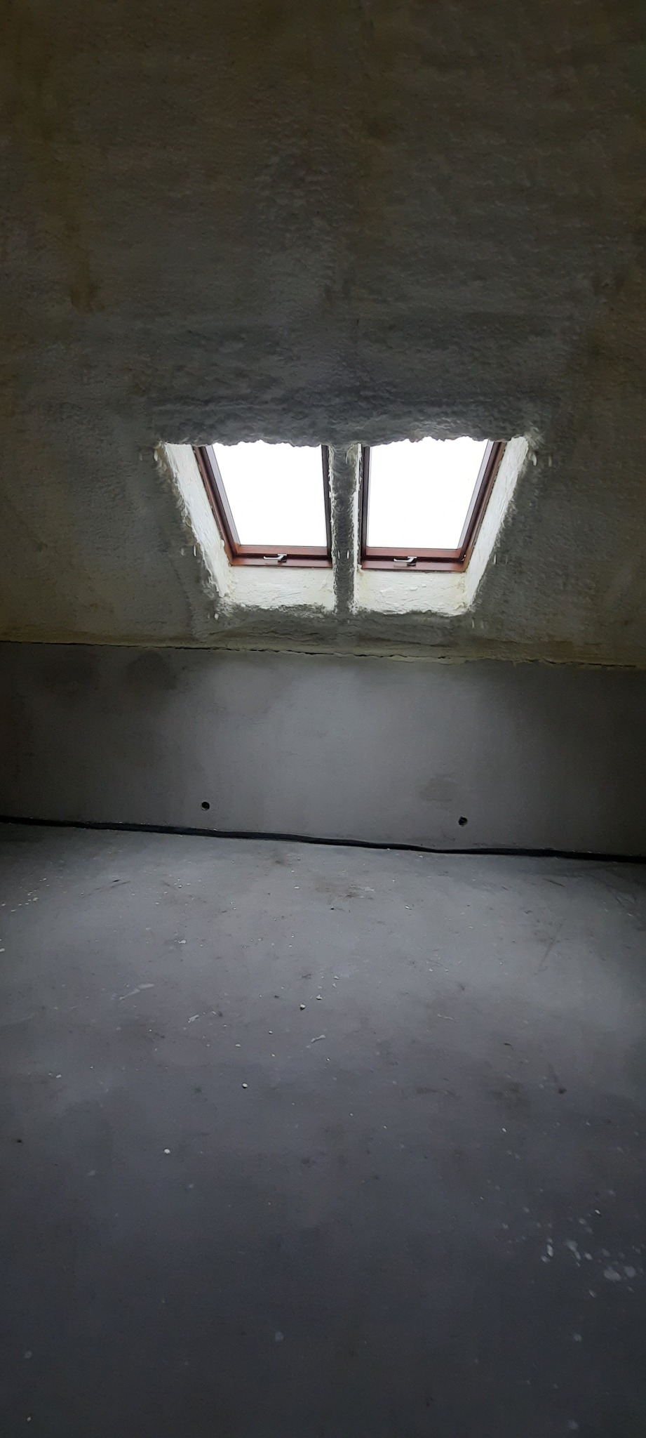 Poddasze z oknami dachowymi, pokryte białą pianką izolacyjną, widok z dołu, szara podłoga.