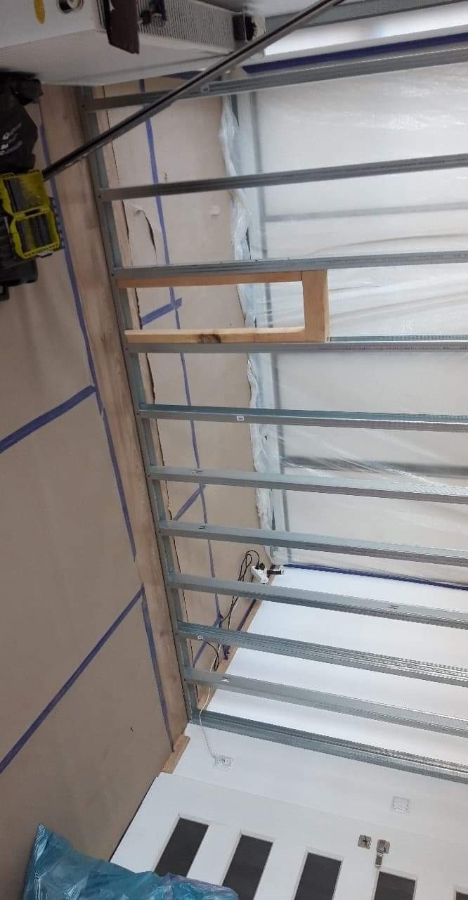 Konstrukcja szkieletowa ze stalowych profili, częściowo obudowana płytą, widoczne przewody elektryczne i narzędzia w tle, przygotowana do dalszych prac wykończeniowych.