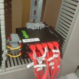 Szczeg&oacute;łowe ujęcie dw&oacute;ch czarnych switchy Wago, z podłączonymi czerwonymi kablami Ethernet oznaczonymi etykietami 'Host-PC' i 'VTD/ADTF', umieszczonych w szafie sterowniczej z szyną montażową...