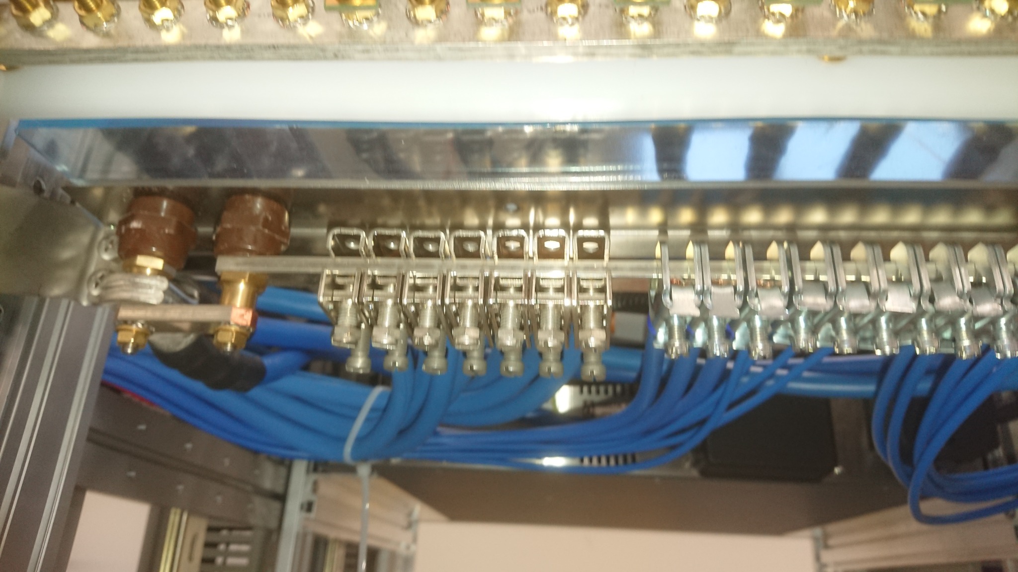 Szczegółowe ujęcie rozdzielnicy elektrycznej z licznymi złączami i niebieskimi kablami, widoczne brązowe elementy izolacyjne i metalowe szyny.