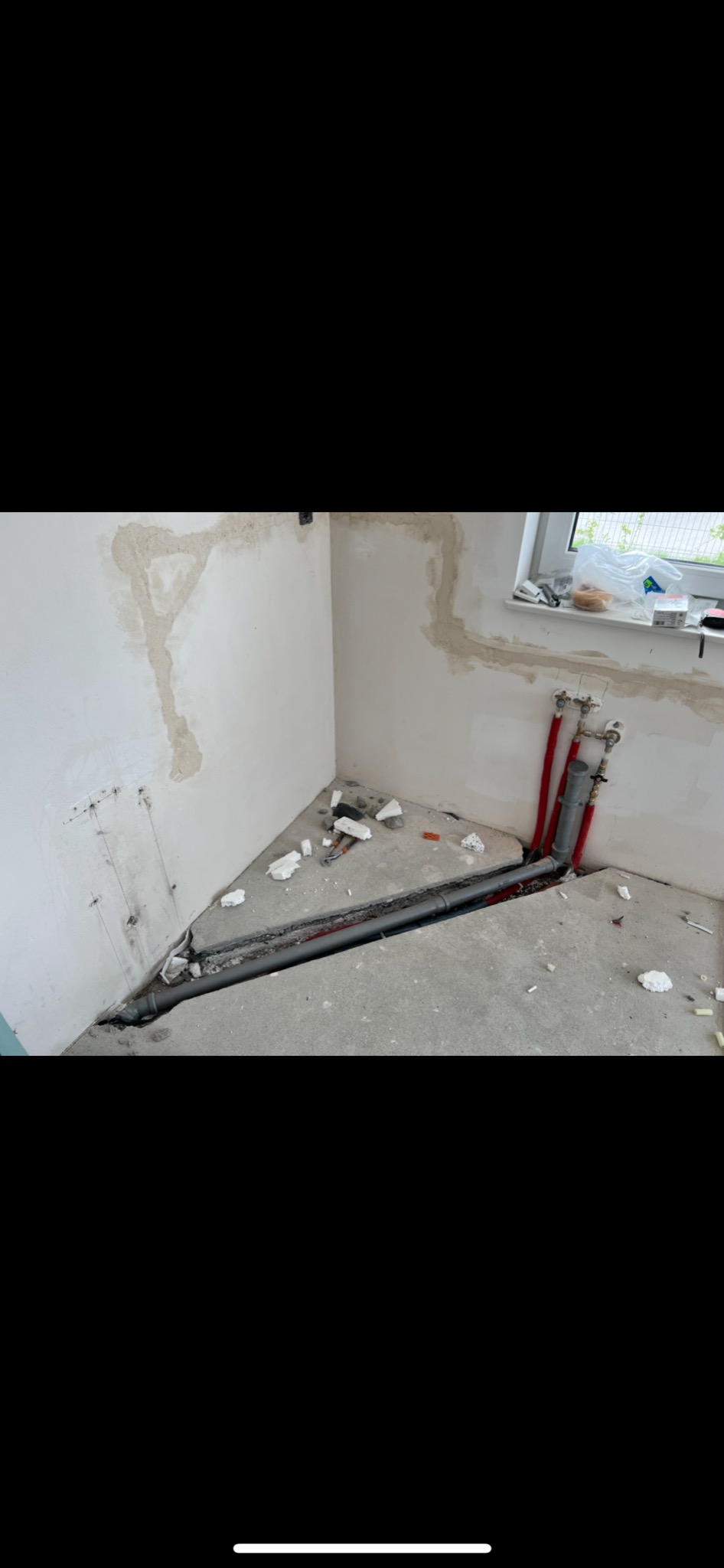 Wykute bruzdy w posadzce pod rury w trakcie remontu łazienki, widoczne wystające rury miedziane, częściowo otynkowane ściany i gruz.