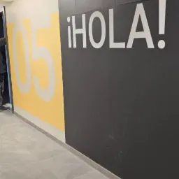 Ściana z napisem '¡HOLA!' i numerem '05' w nowoczesnym biurze. Kontrastowe kolory: czarny, biały i żółty. Minimalistyczny design i sufit rastrowy.