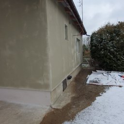 Usługi Remontowe Marcin Frączak - Świeżo otynkowana elewacja domu jednorodzinnego w zimowej scenerii, widoczne ślady po tynkowaniu, brązowe rynny i fragment ośnieżonego trawnika.