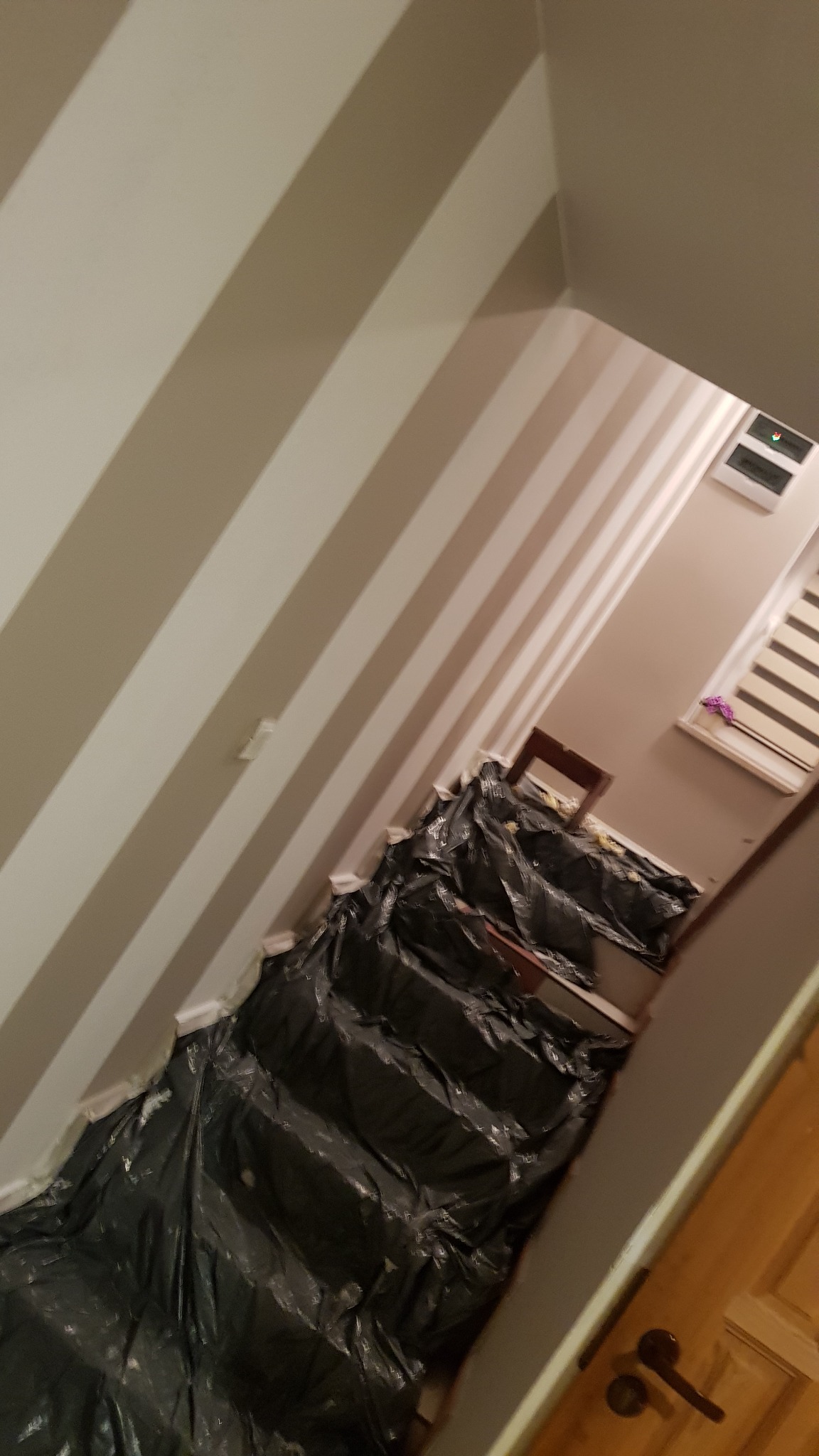 Świeżo pomalowana klatka schodowa w biało-szare pasy, zabezpieczona folią malarską podczas prac wykończeniowych.