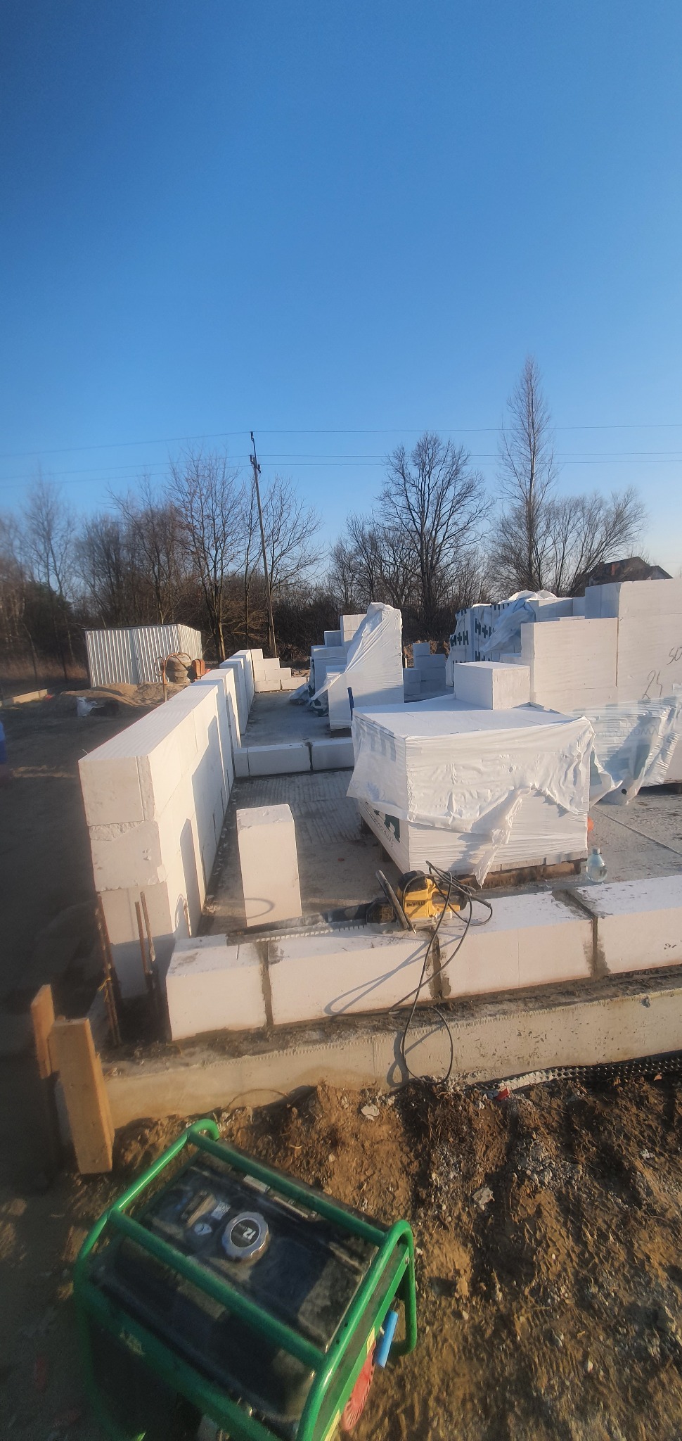 Wznoszenie ścian parteru domu z bloczków betonu komórkowego Ytong, widoczna piła elektryczna do cięcia bloczków i agregat prądotwórczy na ziemi.