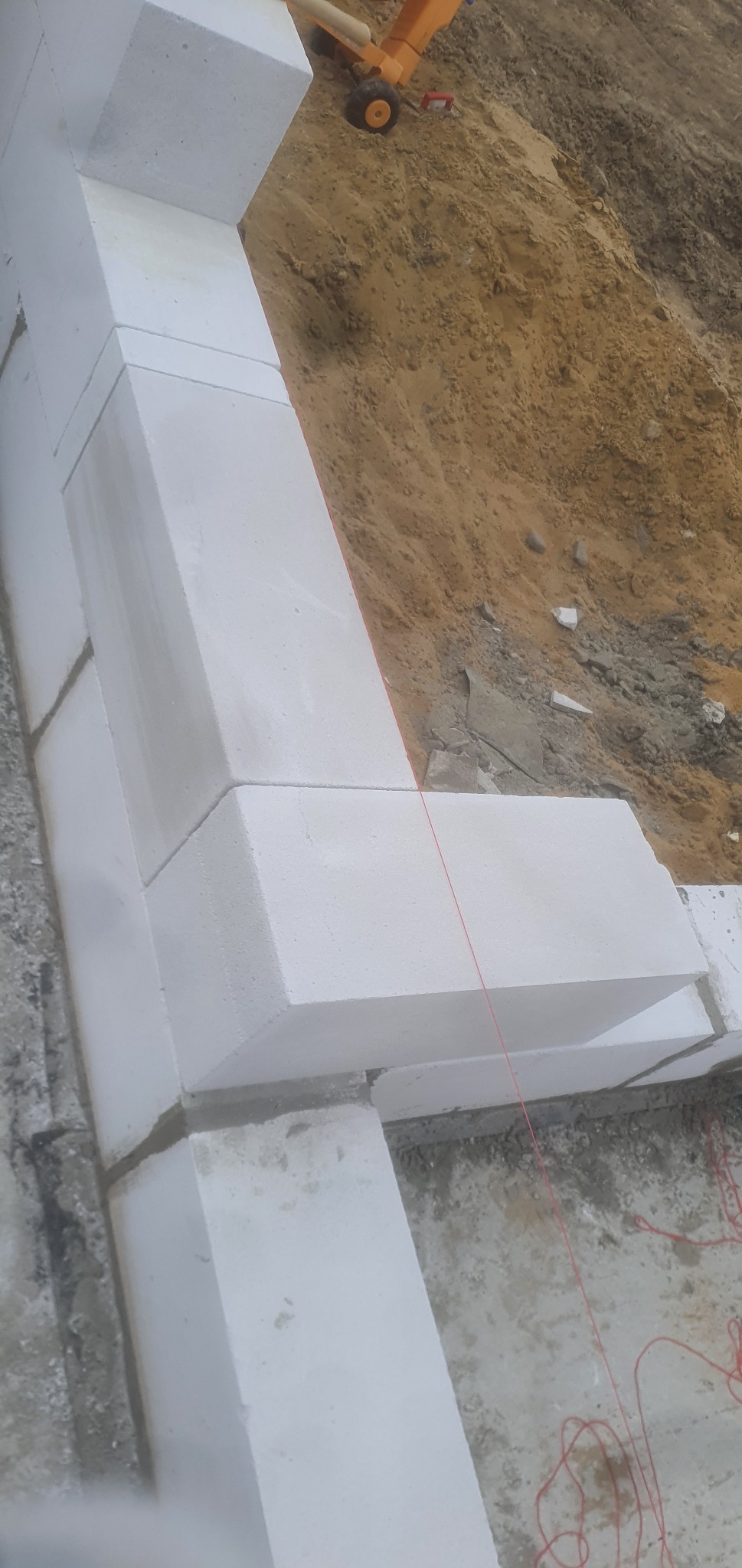 Wznoszenie muru z bloczków betonu komórkowego, widoczna czerwona linka wyznaczająca linię, ziemia w tle.